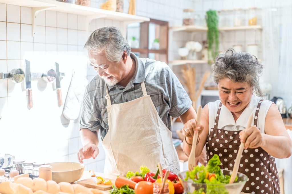 Asian senior elderly grandfather cooking salad dish with grandmother in kitchen with happiness